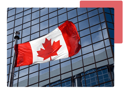 close up of Canadian flag flying in front of an office skyscraper with wall to wall glass windows