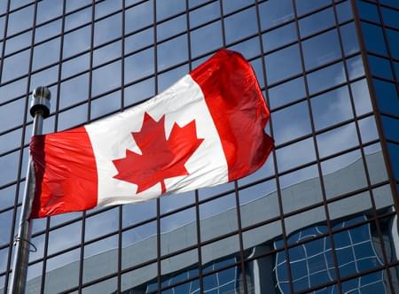 canadian flag flying on flag pole in front of sky scraper office building with wall to wall glass windows