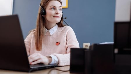 A woman with a headset in front of a laptop looking away from the laptop into the distance - net2phone Canada - Business VoIP Phone System