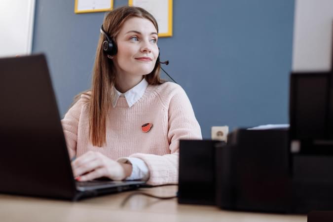 A woman with a headset in front of a laptop looking away from the laptop into the distance - net2phone Canada - Business VoIP Phone System