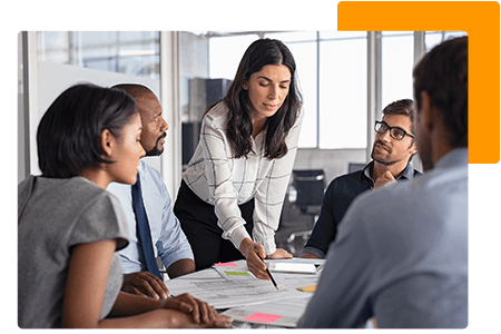 Woman pointing at papers on desk beside employees in office - net2phone Canada - Business VoIP Phone System