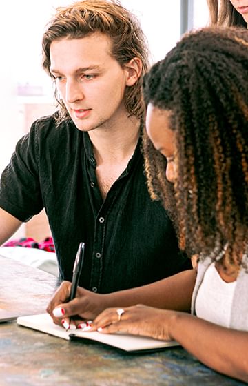 People having a meeting in front of a computer, one woman taking notes