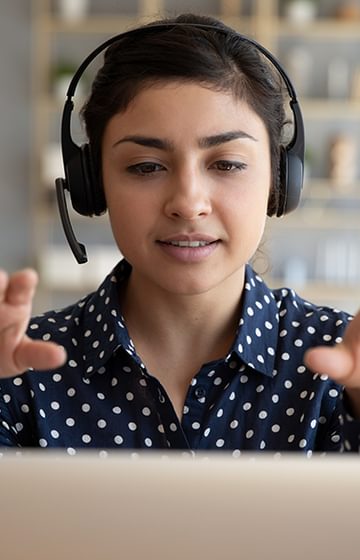 woman wearing a headset on a laptop video call gesturing forward and upward with both hands