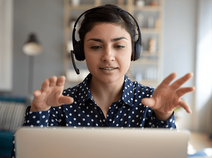 woman wearing a headset on a laptop video call gesturing forward and upward with both hands