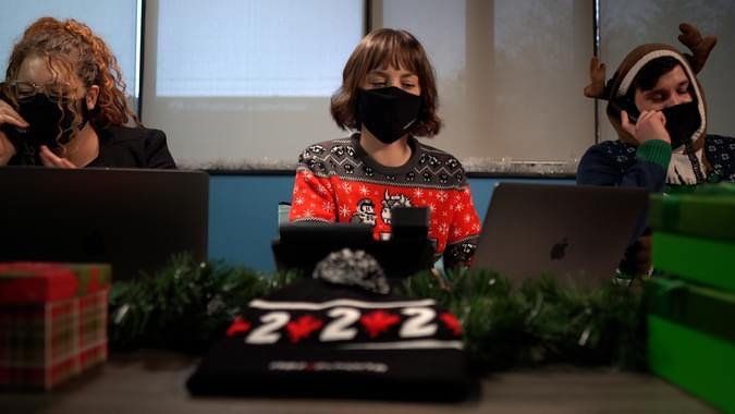 Three people wearing masks at the same table the two outside people are on desk handsets and the middle person is on her laptop - net2phone Canada - Business VoIP Phone System