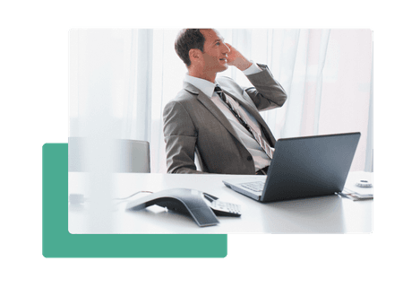 man in suit sitting at desk talking on phone in front of conference phone and laptop - net2phone Canada - Business VoIP Phone System