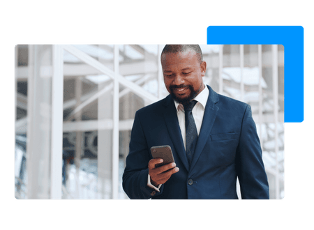 man in suit standing in front of modern office smiling while looking at smart phone