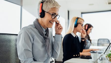 three women in business attire with headsets working in a call centre seated in front of laptops