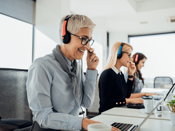 three women in business attire with headsets working in a call centre seated in front of laptops