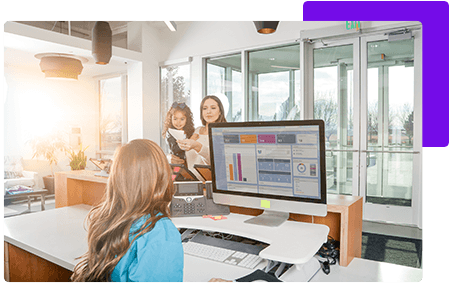 Woman at receptionist desk in front of computer talking to female client holding child - net2phone Canada - Business VoIP Phone System