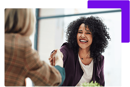 Woman with black hair shaking hands with woman in brown blazer in office - net2phone Canada - Business VoIP Phone System