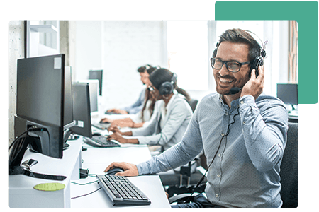 Man working at desk laughing in headset looking at computer beside employees - net2phone Canada - Business VoIP Phone System