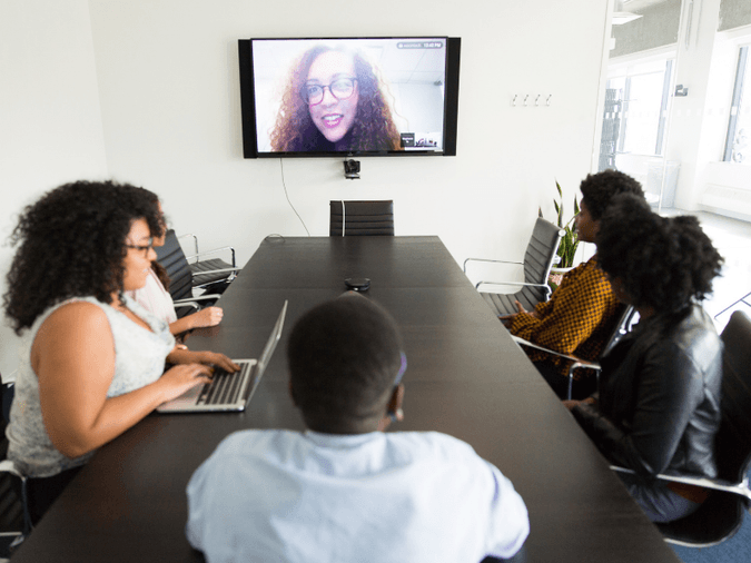 employees around a boardroom table speaking to a woman on a video call - net2phone Canada - Business VoIP Phone System