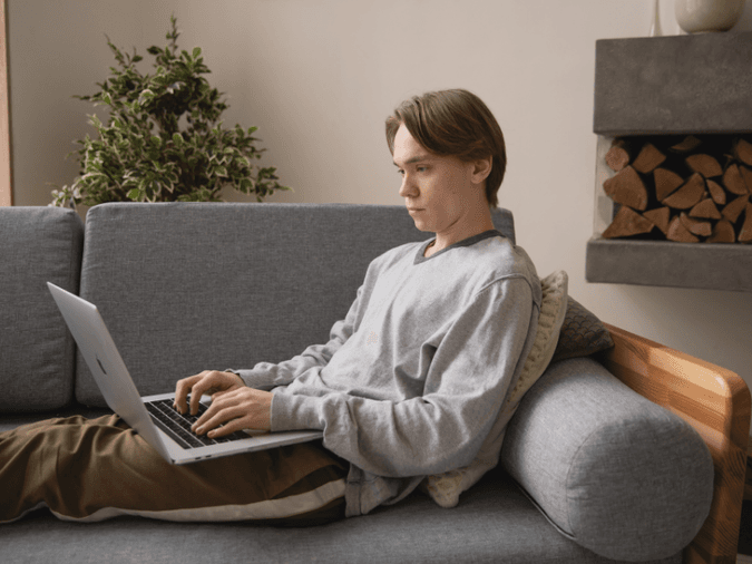 Man sitting on grey couch with laptop - net2phone Canada - Business VoIP Phone System