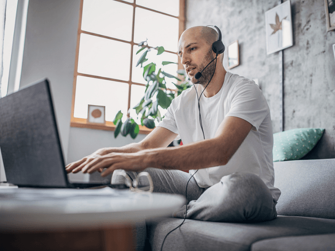 man wearing a headset and typing on a laptop working from home on his couch