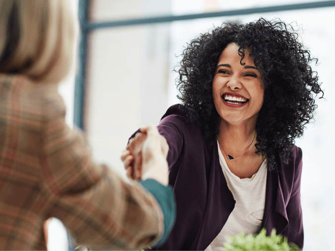 two professional women smiling and shaking hands