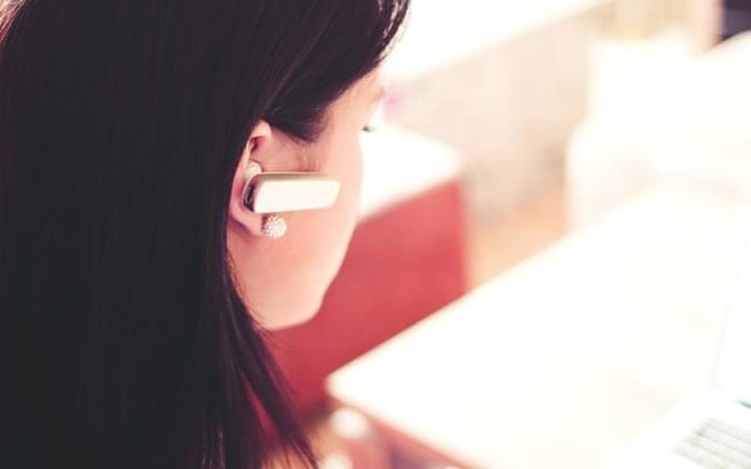 Ear set bluetooth worn by brunette woman - net2phone Canada - Business VoIP Phone System
