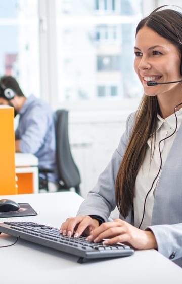 Smiling woman wearing phone headset on desktop computer - net2phone Canada - Business VoIP Phone System