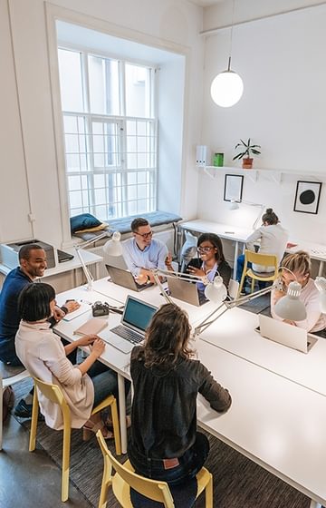 group of people working around a large table in a modern open concept shared office space