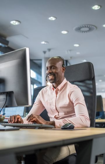 man speaking on headset in front of computer in open concept office