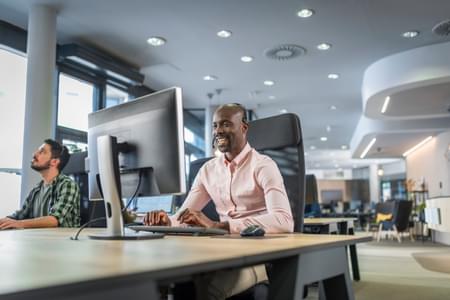 man speaking on headset in front of computer in open concept office