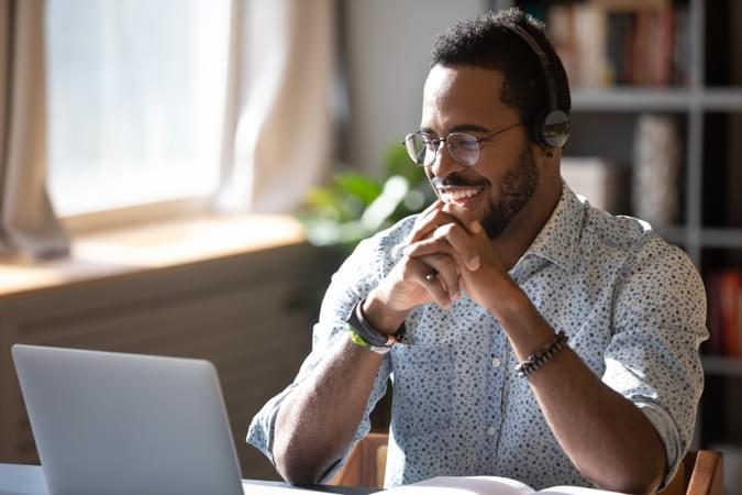 man with headset on smiling while seated in front of laptop in home office