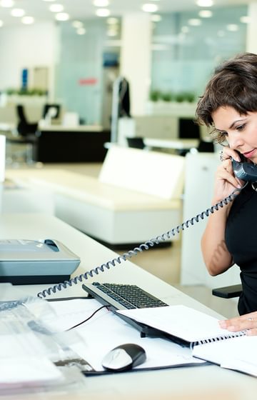 business woman reading a document in front of her laptop while speaking on a desk phone