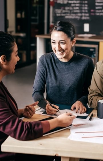 Man and two women sit at light wood table overlooking papers - net2phone Canada - Business VoIP Phone System