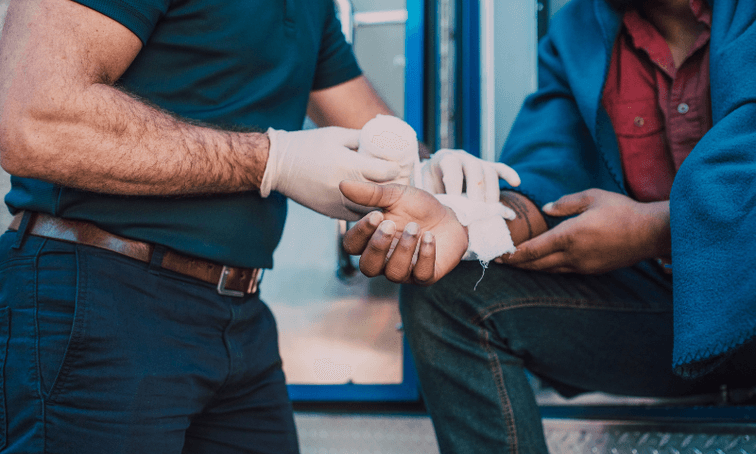 First responder wrapping another man's arm sitting on ambulance due to injury