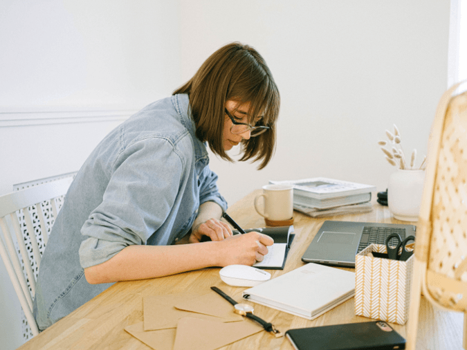 A woman writing something in a note book in front of her laptop - net2phone Canada - Business VoIP Phone System