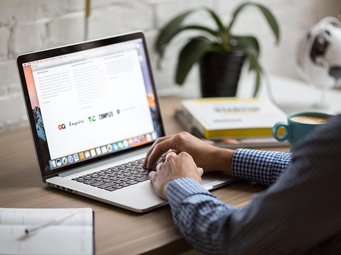 Man using apple laptop on wooden desk with plant - net2phone Canada - Business VoIP Phone System