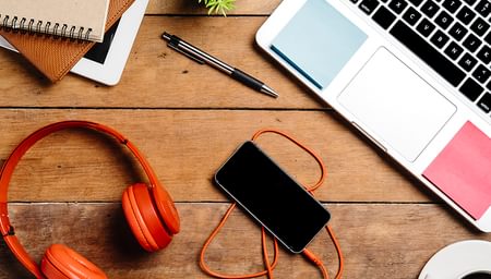 headphones, a phone, a pen, notebooks, and a laptop on a desk