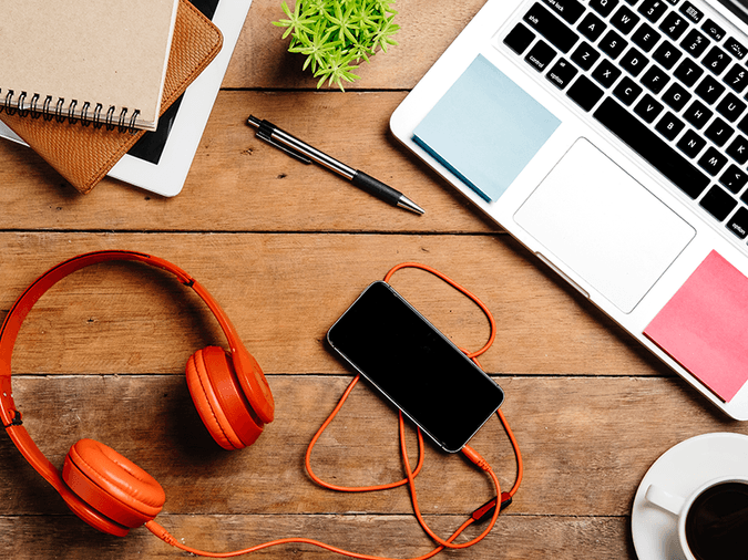 headphones, a phone, a pen, notebooks, and a laptop on a desk