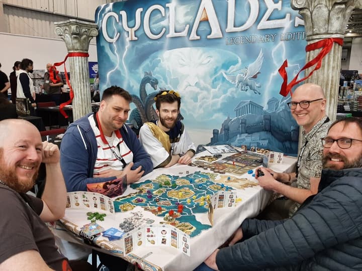 A group of people playing the Cyclades board game at a board game show.