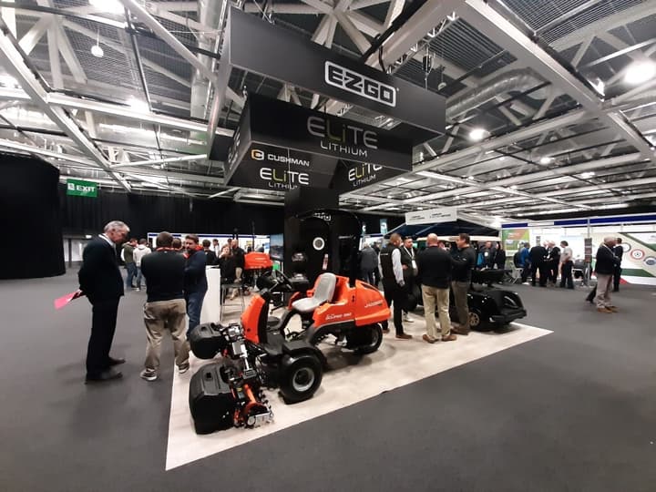 People gathering around a stand displaying vehicles in a large exhibition hall