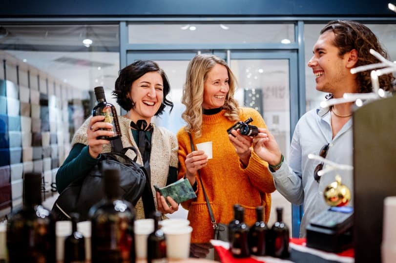 Two ladies and one man smiling at each other over a table full of bottled beverages