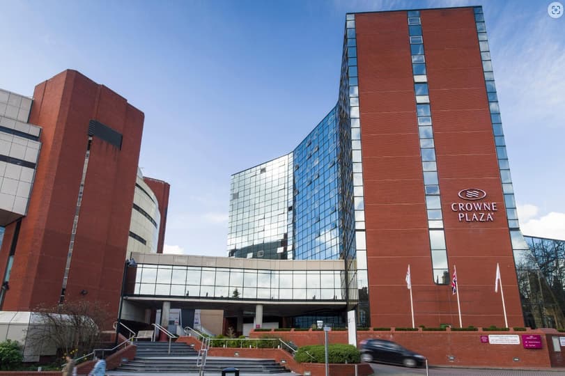 A modern glass facade hotel building connected by a footbridge to an auditorium