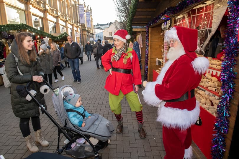 Woman in elf costume and Santa Claus greats woman pushing a baby at Harrogate Christmas Fayre