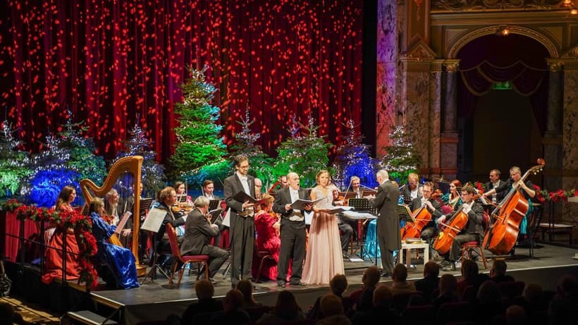 Singers perform with orchestra on stage in front of Christmas trees