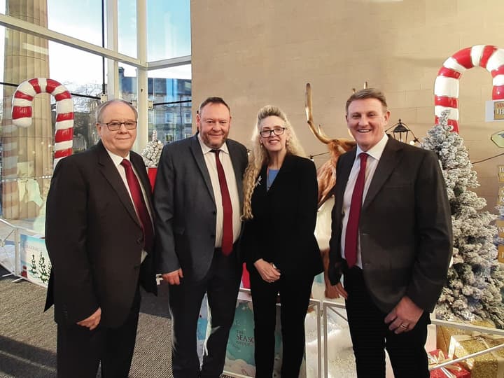 3 men and 1 woman in business attire standing in front of Christmas decorations