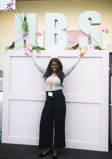 A woman smiling and posing with her arms raised in front of a Harrogate Bridal Show backdrop