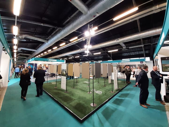 People in business attire walking around a stand displaying flooring material in an exhibition hall