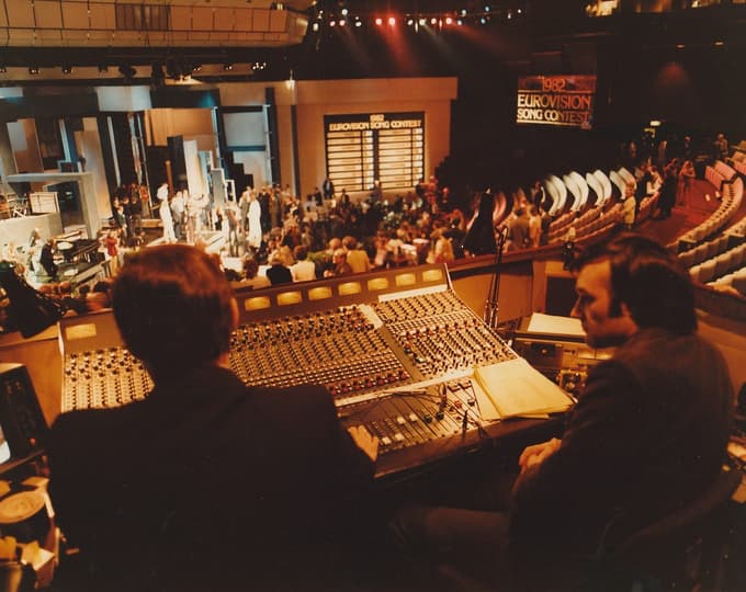 2 men sitting at a mixing desk in an auditorium with performers on stage