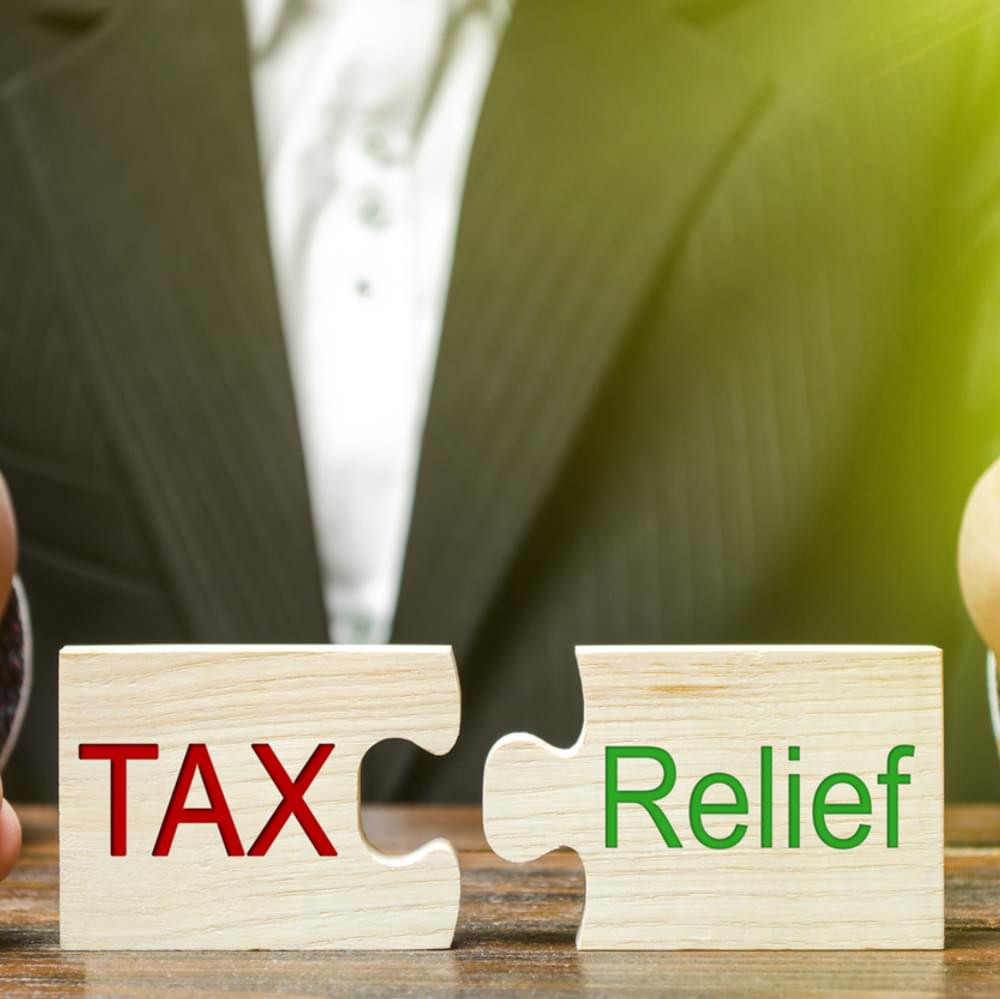 A businessman puts two puzzles with the words Tax and Relief. The concept of reducing the debt burden on business and local production to increase the competitiveness of their products. Economy stock photo