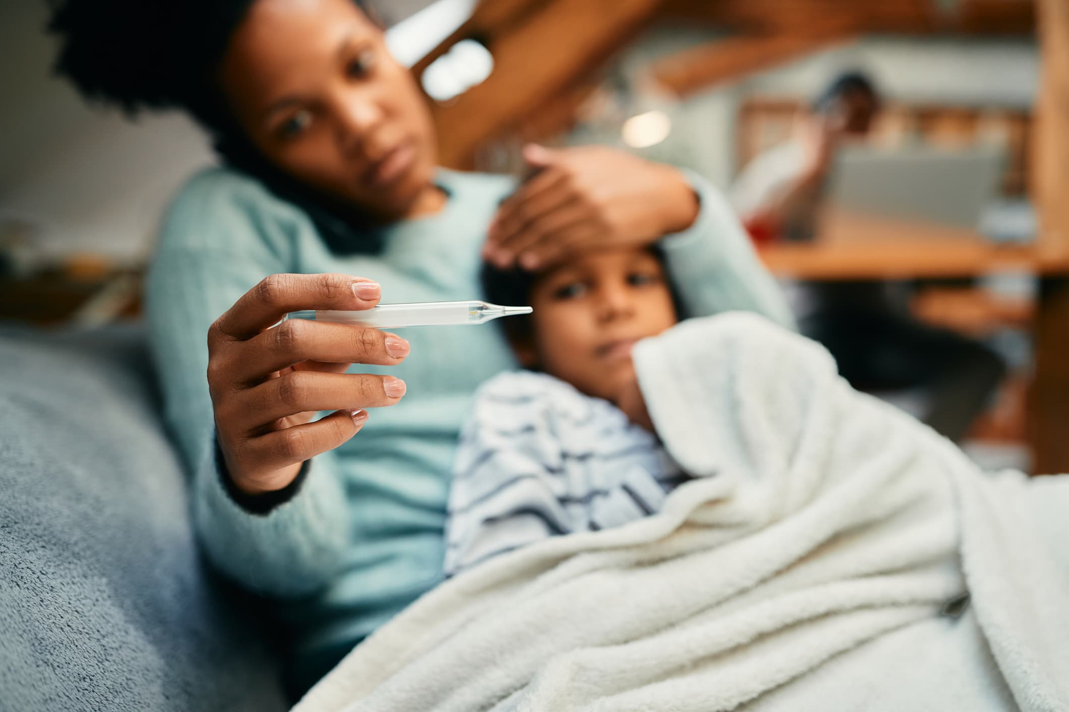 Close-up of African American mother using thermometer and measuring temperature or her sick son at home.