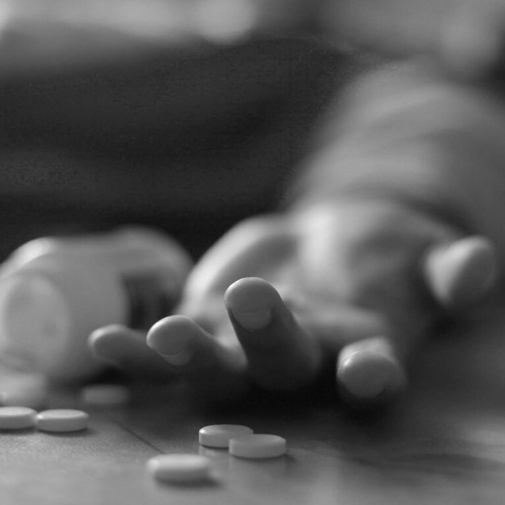 Man lying on the floor, unconscious or dead due to drugs abuse, focus on fingers with pills stock photo Alabama News