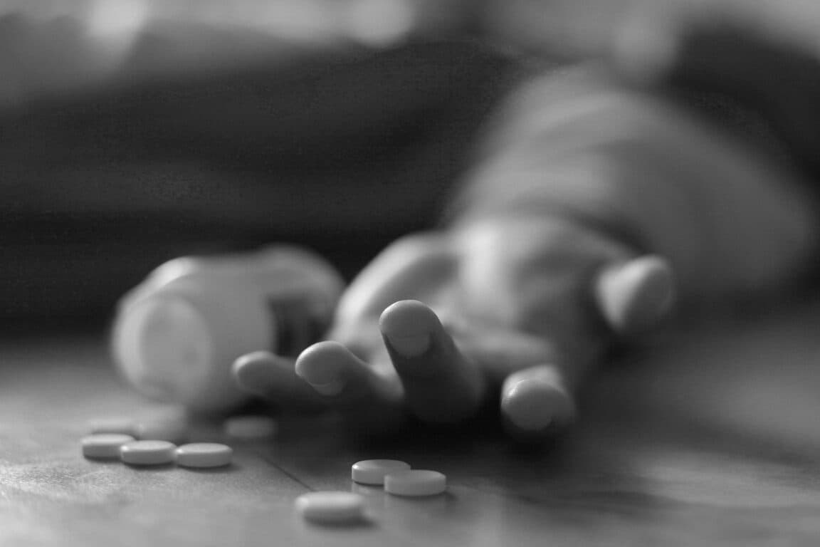 Man lying on the floor, unconscious or dead due to drugs abuse, focus on fingers with pills stock photo