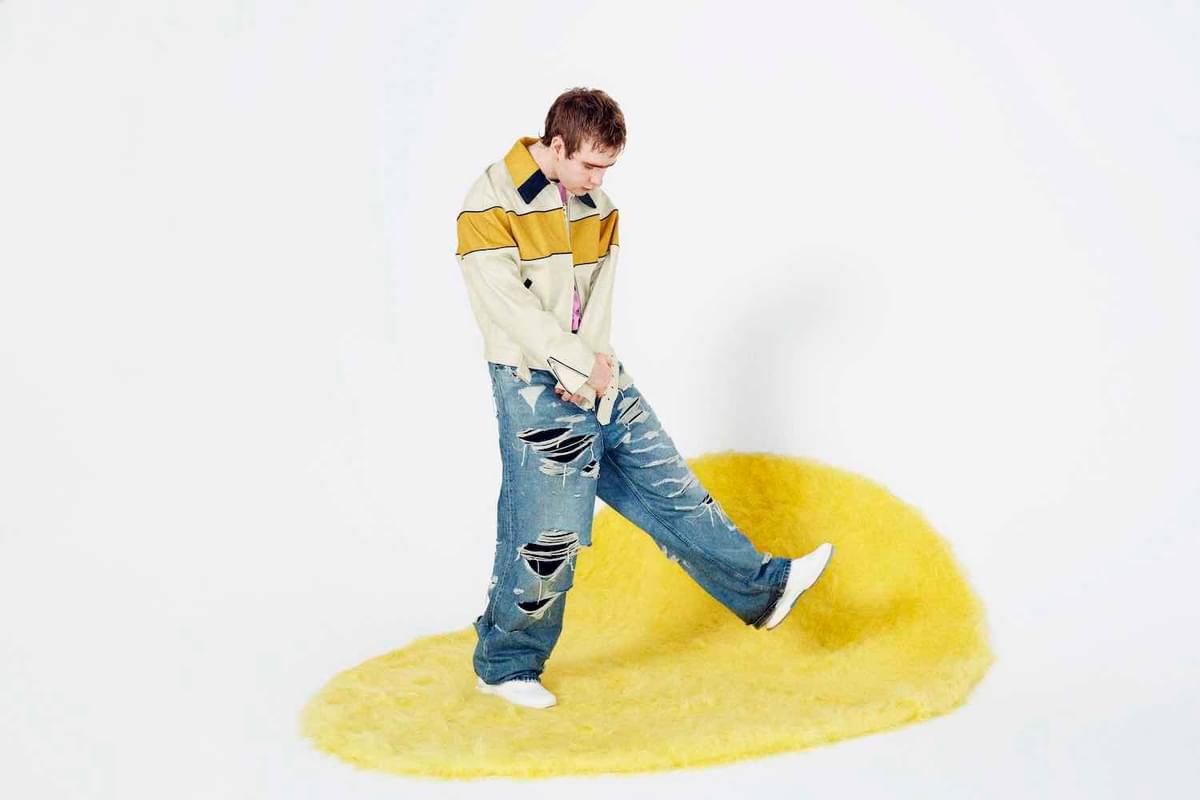 Mura Masa walking on a yellow rug for "e-motions" single