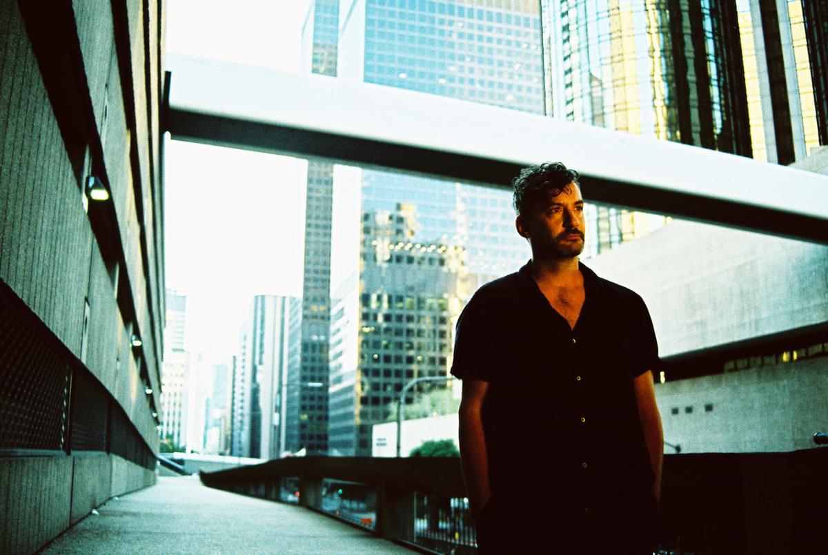 Bonobo stood on a concrete walkway under skyscrapers for "ATK" single