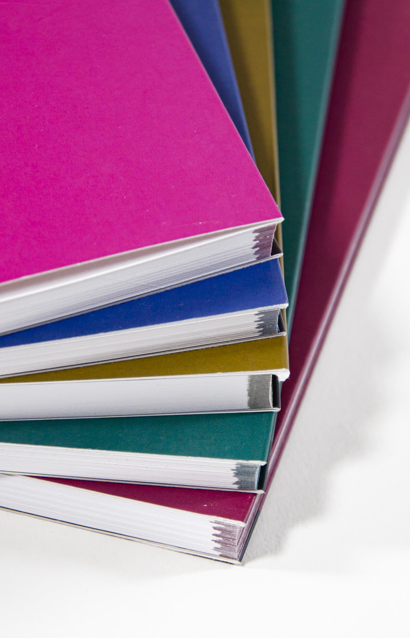 Bildet viser fem bøker som ligger oppå hverandre i en vifte. Alle har ulik farge på omslaget og i ytterkanten. Fra toppen: rosa, mørkeblå, grumsete grønn, mørkegrønn og burgunder